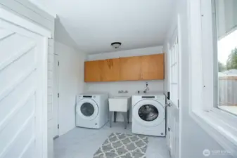 Cheerful laundry/mudroom - pantry in foreground, brand new luxe vinyl tile floors, access to garage at left and to back yard at right.