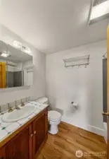 Apartment 7 Bath – Fresh, Functional, and Bright  Apartment 7’s full bath combines utility with warmth—featuring updated fixtures, a large vanity with storage, and hardwood floors that carry through from the main living space. A skylight above adds natural light, completing this clean and comfortable retreat within one of Laurel Gate’s most distinctive homes.