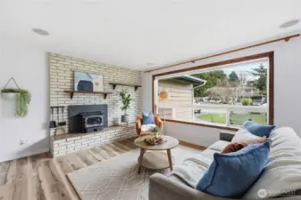 Bright and welcoming living room featuring a cozy wood-burning stove, newly installed luxury plank vinyl flooring, and abundant natural light from the expansive bay window.