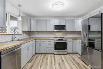 Stylishly remodeled kitchen with butcher block countertops, mosaic tile backsplash, new cabinetry, stainless steel appliances, and luxury plank vinyl flooring for a seamless transition from the living room.