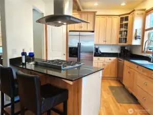 Breakfast bar overlooks stainless steel gas stove with custom stainless hood. Your guests can keep you company while you are preparing a feast.