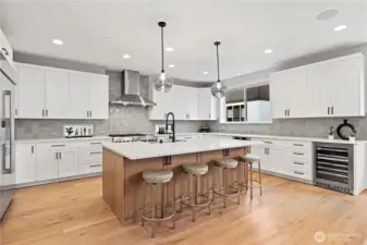 Showstopping chef’s kitchen featuring an oversized island, JennAir appliances, luxe tile backsplash, quartz counters, and abundant cabinetry storage.