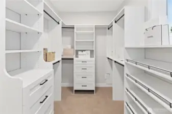 Spacious primary suite walk-in closet with custom built-ins, generous hanging space and shelving, shoe shelves, two banks of drawers, and a window brings in natural light.