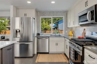 Updated kitchen with ceramic tile floors, quartz countertops, marble tile accent backsplash, shaker cabinets, and a full suite of stainless steel appliances, including a built-in microwave and a 5-burner gas range.