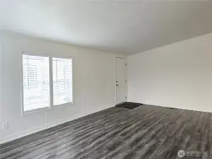 Spacious and inviting living room filled with natural light from windows on two walls, creating a bright and airy feel. Blinds are already in place for privacy and light control, making this space both comfortable and move-in ready.
