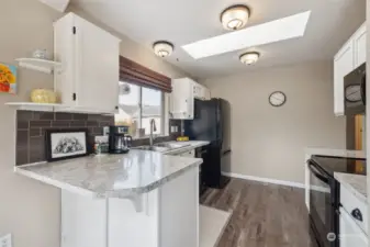White and bright kitchen with tiled backsplash and skylight, plus all appliances stay!