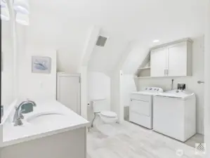 This updated main-floor second bathroom doubles as a laundry space and features a custom cabinet with silestone countertops and durable and elegant LVP flooring.