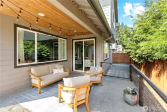 Covered back patio with lights and railings leads around the house for additional gated outside storage