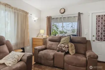 Step into a warm and inviting living room, bathed in natural light filtering through dual windows. This space is designed for relaxation, perfect for unwinding after a long day. Thoughtful touches like a subtle wall sconce and charming built-in shelving enhance the cozy atmosphere. A perfect blend of comfort and function!