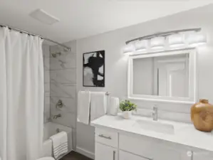 The updated main bath features tiled tub surround, beautiful vanity, mirror, lighting.