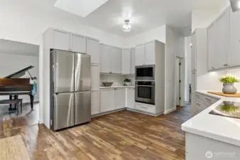 Spacious kitchen with abundant cabinetry, sleek white quartz counters, stainless steel appliances, a dry bar, generous natural light, and an open layout for easy movement.