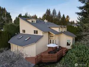 Exterior view of the expansive home featuring a spacious multi-level welcoming deck, mature landscaping, and a peaceful wooded backdrop.