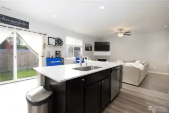 Open concept kitchen with quartz counters, rich cabinetry looks out to dining and sliding door leading to fully fenced yard