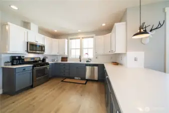 View 2 of spacious kitchen with quartz countertops, engineered wood floors, stainless steel appliances and gas stove.