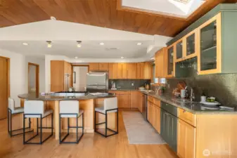 A spacious, well-designed kitchen featuring a generous island with bar seating, warm wood cabinetry, and a striking slatted wood ceiling that adds architectural character — offering ample room for cooking, gathering, and entertaining in equal measure.