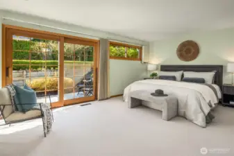 A serene and spacious primary bedroom retreat featuring plush carpet, expansive sliding glass doors that flood the room with natural light and frame lush garden views — a calm, beautifully updated sanctuary perfectly designed for rest and relaxation.