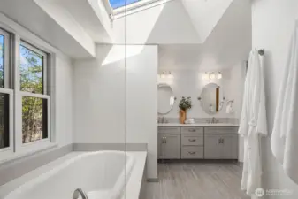 A spa-caliber primary bathroom featuring a luxurious soaking tub beneath a dramatic skylight, elegant dual vanity, and crisp white finishes throughout — a beautifully reimagined space that strikes the perfect balance between indulgence and refined simplicity.