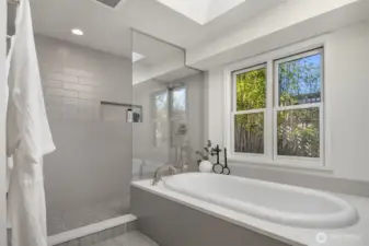 A beautifully updated primary bathroom showcasing a sleek walk-in shower with custom tile, a deep soaking tub framed by sun-filled windows looking out onto a serene, private bamboo garden — sophisticated grey and white finishes completing a spa-inspired retreat thoughtfully designed for everyday luxury.