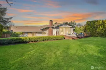 A sweeping view of the beautifully landscaped backyard showcasing the home's classic exterior, expansive flat lawn, and mature trees — a rare and generous outdoor space that perfectly balances privacy, natural beauty, and endless potential for outdoor living.