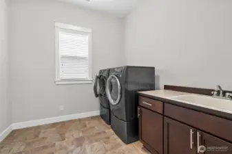 This spacious utility room is as functional as it is bright, thoughtfully designed to simplify everyday tasks. It comes fully equipped with a large washer and dryer, a built-in sink for added convenience, counter space, and ample storage cabinets to keep everything neatly organized. A large wood-wrapped window fills the room with natural light, creating a warm and welcoming workspace that blends utility with style.