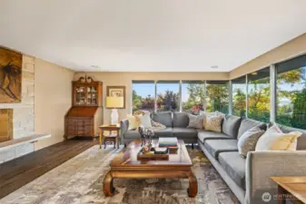 Sunlit living room with cozy fireplace and floor to ceiling windows.