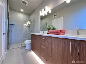 Primary bedroom en suite with glass fully tiled shower, under cabinet lighting, and dual vanity