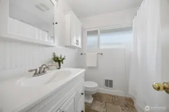 There is a recently updated full bath on the main floor with all white cabinets and fixtures and the stone tile floor similar to that in the kitchen and dining areas.