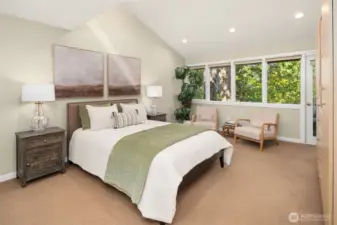 Luxurious primary bedroom featuring vaulted ceiling, wall of windows and door to private deck,