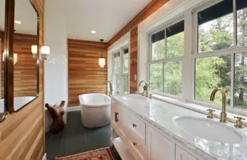 Radiant floor heat adds to the warmth of the fir paneled walls in your primary bathroom. Double sinks with a view. The tiled wall to the left of the soaking tub belongs to the shower and the toilet is around the corner adjacent to the shower.