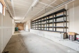 3 car tandum garage with high ceilings, shelving and tall doors at each end.