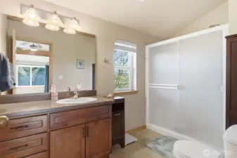 A serene primary three-quarter bath blends clean design with natural warmth. The space features a spacious walk-in shower enclosed in frosted glass.