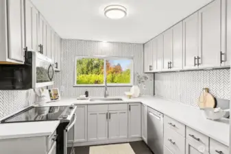 Stunning renovated kitchen at 4612 N 21st St, Tacoma, WA — showcasing quartz countertops, full herringbone tile backsplash, soft-close shaker cabinets, stainless steel appliances, and a large window with vibrant backyard views. This bright and spacious North Tacoma kitchen offers modern finishes, abundant storage, and a functional L-shaped layout perfect for cooking and entertaining.