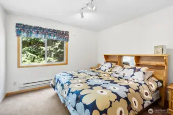 Sunlit bedroom with large window and peaceful treetop views.