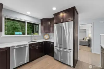 Modern kitchen with stainless steel refrigerator, dishwasher, and dark wood cabinetry, offering generous prep space and natural light.