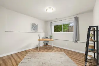 Additional bedroom or office with wood-look flooring, bright window, and flexible use for remote work or guest space.
