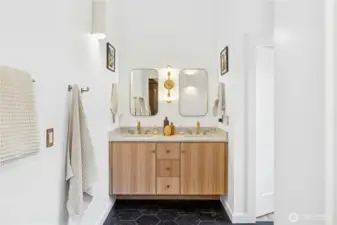 The spa-inspired primary bath features a custom double vanity with beautiful countertops, warm wood cabinetry, and designer brass fixtures. Clean lines and curated lighting create a fresh, elevated feel. Perfect for unwinding at the end of the day.