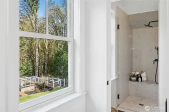 The primary bath continues the spa aesthetic with a luxe walk-in shower, sleek black fixtures, and timeless stonework. A large window frames tranquil views over the garden and goat pen, bringing the beauty of the property right into your daily routine.