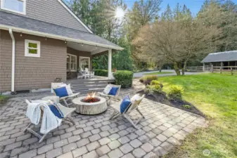 A paver patio with built-in fire pit extends the living space outdoors, framed by mature landscaping and a welcoming covered porch. Enjoy golden-hour gatherings with easy sightlines to the barn and fenced pasture. Perfect for entertaining while staying connected to the heart of the property.