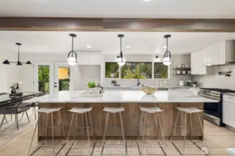 The centerpiece of the kitchen is an expansive quartz-slab island with abundant seating, convenient outlets, and extensive storage cabinetry. Overhead, modern black-framed pendant lights with glowing globe shades add a sophisticated touch, perfectly complementing the island’s elegant design.