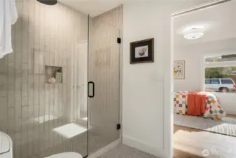 A frameless glass door showcases the tiled floor and designer tiled walls. The second door leads to the front bedroom.