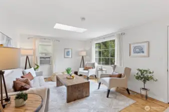 Another view of the large living room space with picture window, oak flooring and skylight.