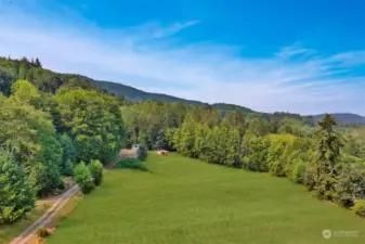 Driveway to left, exiting the property. Small homestead in the distance before gated entry.