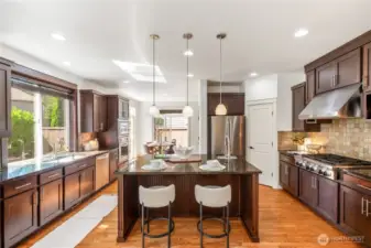 Chef's kitchen with granite countertops, center island w/ veggie sink, 6-burner gas stove, full-height backsplash, stainless steel appliances.