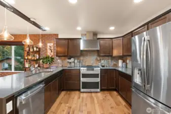 This chef-inspired kitchen blends elevated design with thoughtful functionality. A professional-grade stainless-steel range with double ovens and gas cooktop anchors the space, complemented by a sleek vented hood that enhances both performance and style. The French-door refrigerator with built-in water and ice dispenser adds everyday convenience, while layered lighting — from recessed ceiling fixtures to statement pendants — ensures the perfect ambiance for cooking, dining, and entertaining. Striking accent tile and custom brick veneer detailing add texture and sophistication, beautifully paired with warm cabinetry and quartz-style counters to complete this stunning culinary space.