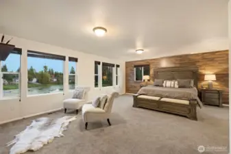 Spacious and serene, the primary suite offers a true retreat from the everyday. The generous proportions of the room — easily accommodating a king-sized bed with plenty of space to spare — create a sense of openness and comfort. Expansive windows flood the space with natural light and capture calming lake views, while the warm wood accent wall adds texture and timeless character.