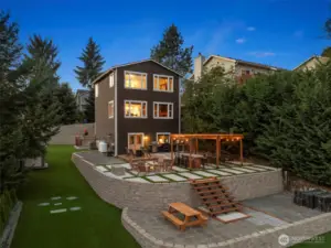 Evening ambiance highlights the layered outdoor design — multiple entertainment zones, easy access to the water, and a seamless indoor-outdoor connection.
