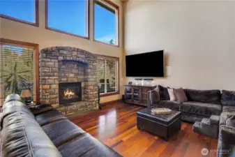 A fireplace enhances the warmth and inviting ambiance this room The fully wood-trimmed windows two-story design frame tree-filled views, integrating the natural surroundings into the space.