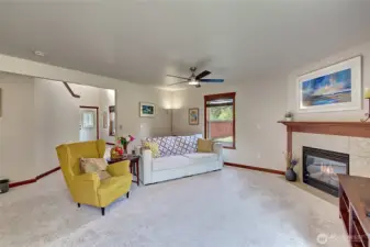 Bright and inviting living room featuring a cozy fireplace and a new ceiling fan for comfort. All-new lighting throughout the home adds a fresh, modern touch. The open floorplan flows seamlessly into the kitchen and dining areas.