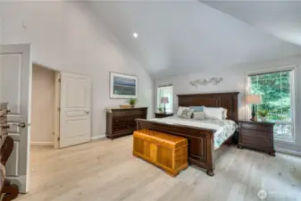 Oversized primary suite with white oak hardwood flooring, french doors, vaulted ceilings, and plenty of sunlight.