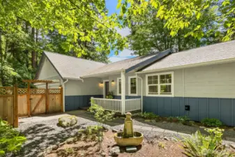 View to the front entry. The gate opens to the paved driveway. The covered front porch is a nice place to sit and take in the garden views.